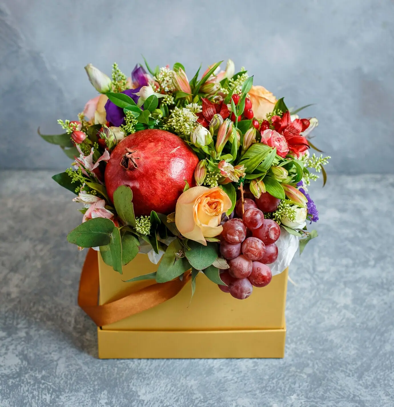 Цветочный букет с гранатом и виноградом в жёлтой квадратной коробке.