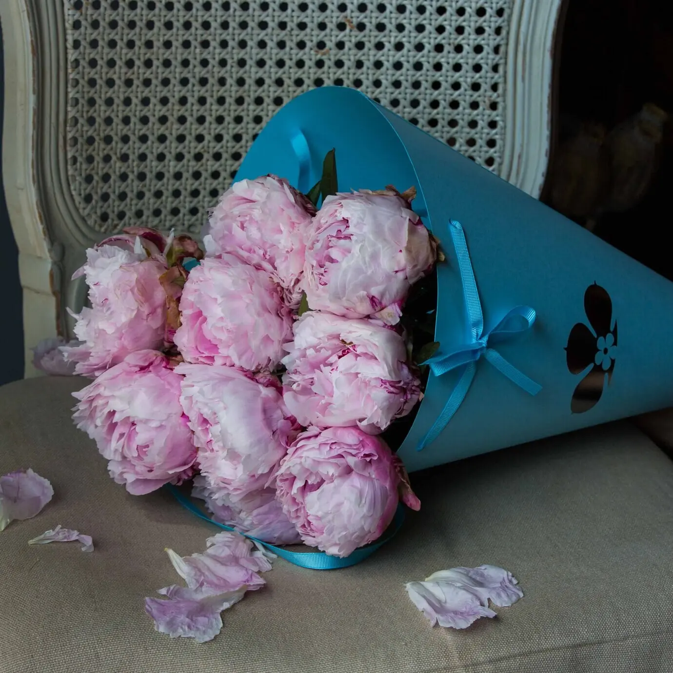 Букет розовых пионов в синем картоне на стуле.
